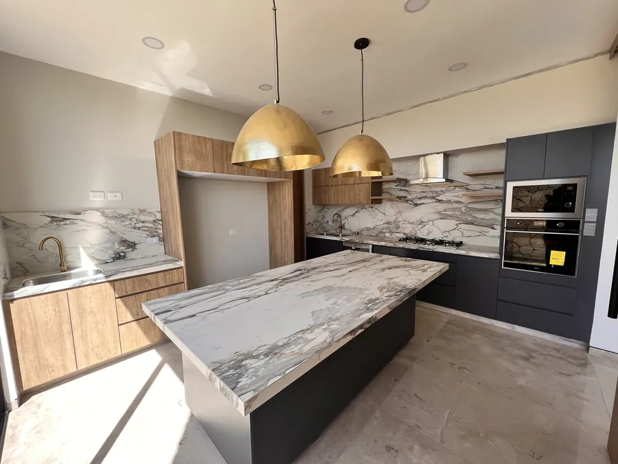 Cocina con isla de mármol tipo cascada y lámparas de latón — penthouse en Lomas de Angelópolis, Puebla